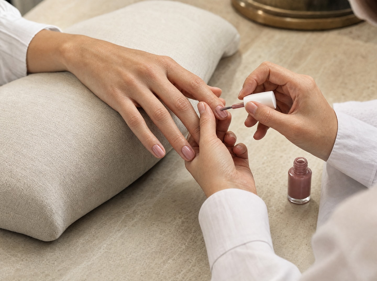 Une manucure rose naturel, réalisée au pinceau sur une main posée sur du lin.
